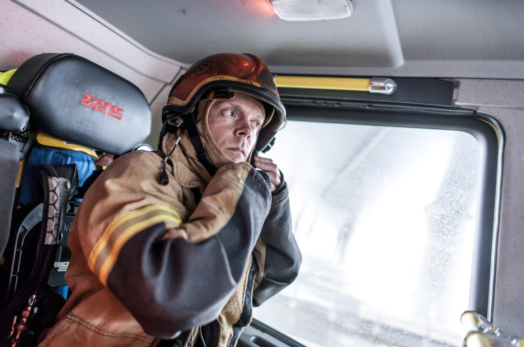 Bilde av brannmann som tar på seg hjelmen mens han sitter i en brannbil.